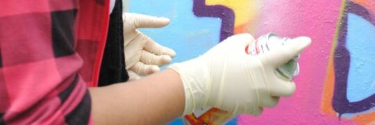 Hand mit Spraydose vor bunter Wand